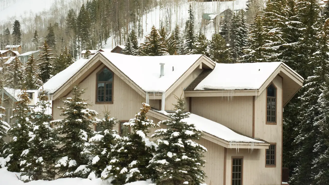 A snow-covered mountain home nestled amidst towering trees, with well-sealed windows, prepared to withstand Colorado's winter weather